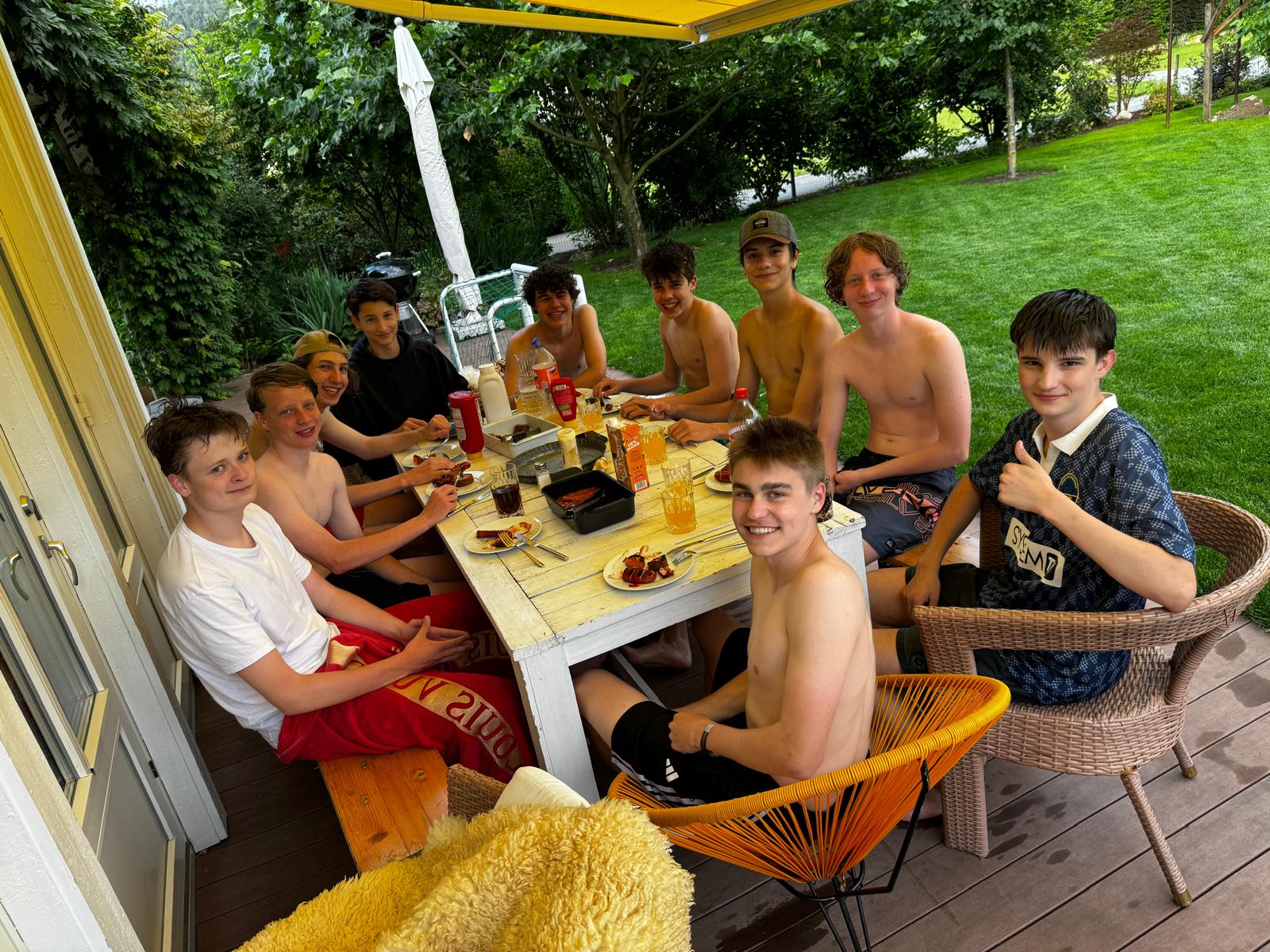 Eine Gruppe Jugendlicher sitzt lachend an einem Tisch auf einer Terrasse beim Grillen
