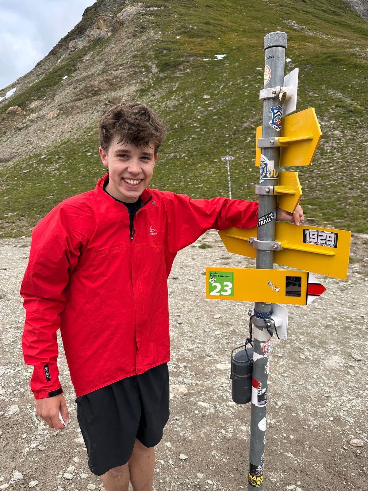 Joris steht lachend neben einem Wegweiser auf einer Bergwanderung