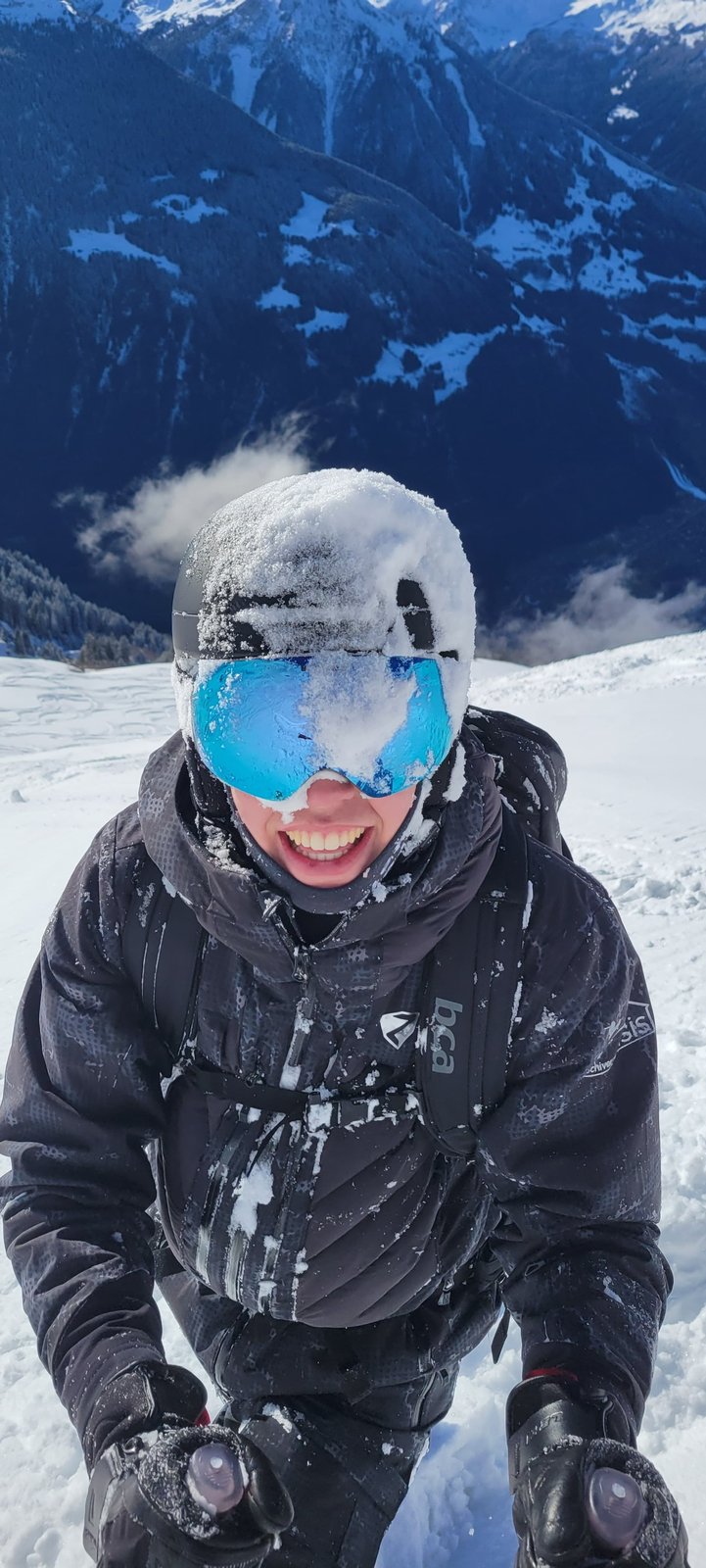 Joris mit schneebedeckter Skibrille und Helm, lachend vor einem winterlichen Bergpanorama